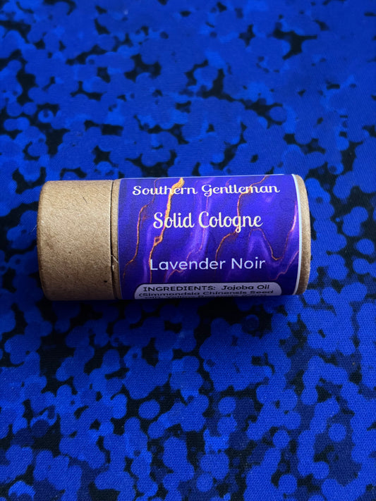 Solid cologne stick with purple "Lavender Noir" label on a blue textured background
